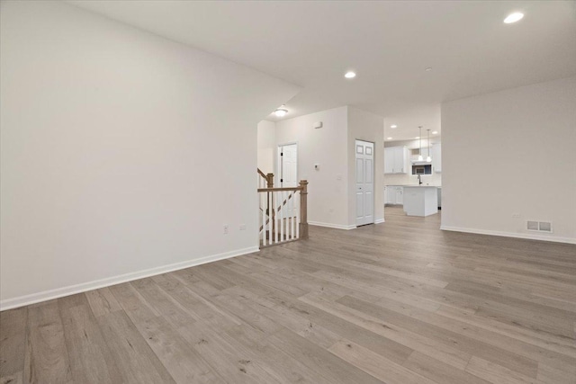 unfurnished living room with baseboards, visible vents, stairs, light wood-type flooring, and recessed lighting