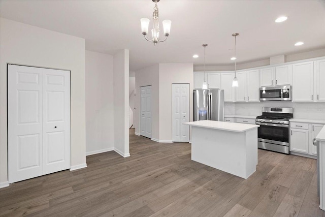 kitchen with white cabinets, a kitchen island, appliances with stainless steel finishes, wood finished floors, and light countertops