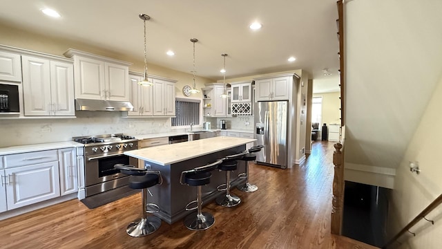 kitchen with under cabinet range hood, appliances with stainless steel finishes, dark wood-type flooring, and a kitchen breakfast bar