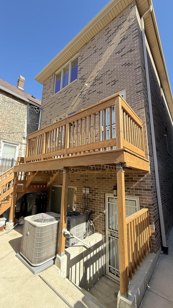 back of house featuring a deck, brick siding, and central AC