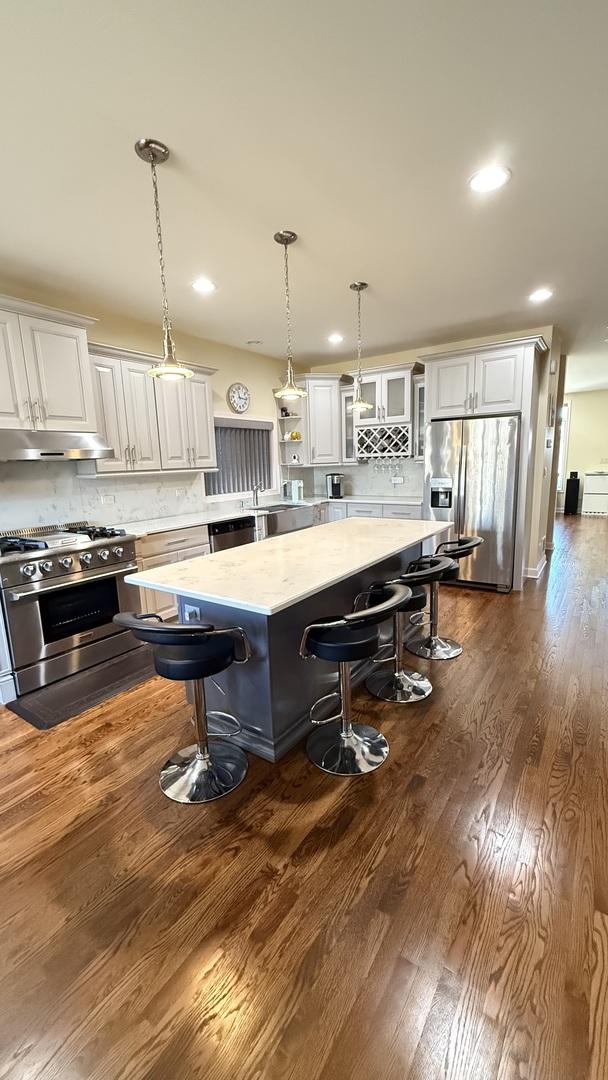 kitchen featuring under cabinet range hood, white cabinets, stainless steel appliances, and a kitchen bar