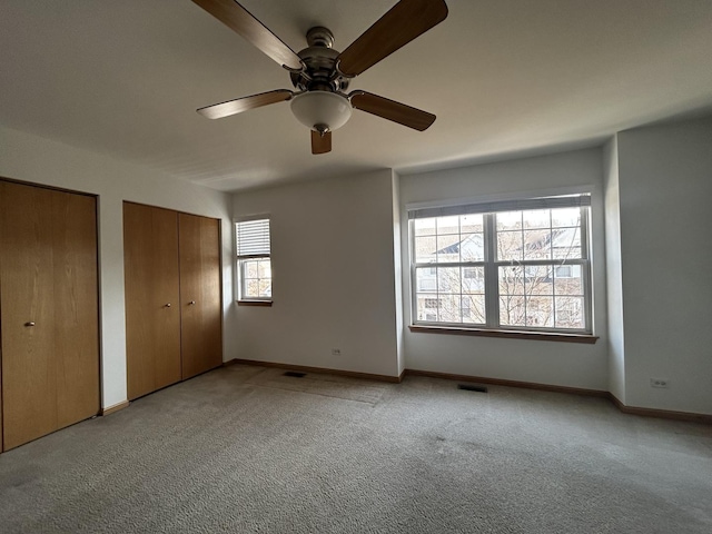 unfurnished bedroom with baseboards, carpet flooring, two closets, and visible vents