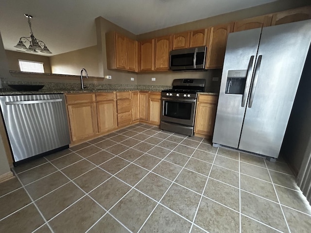 kitchen with tile patterned flooring, dark stone countertops, appliances with stainless steel finishes, and a sink