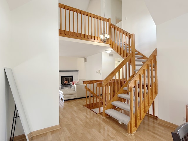 stairs featuring a notable chandelier, wood finished floors, visible vents, a towering ceiling, and a brick fireplace