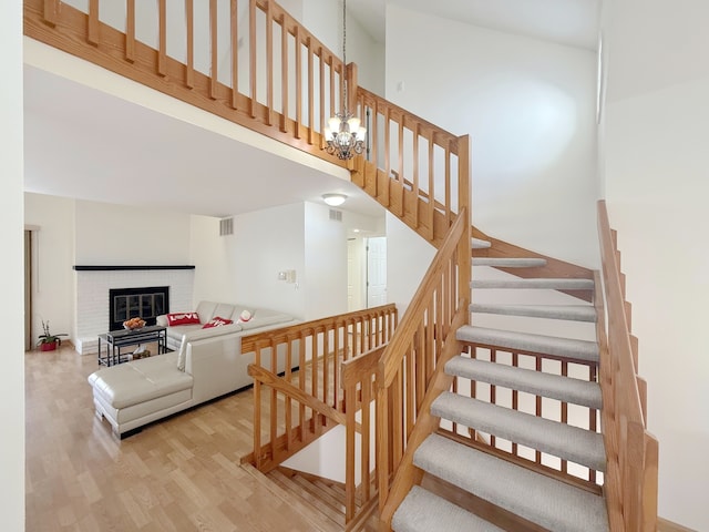 stairs featuring visible vents, a high ceiling, an inviting chandelier, a brick fireplace, and wood finished floors