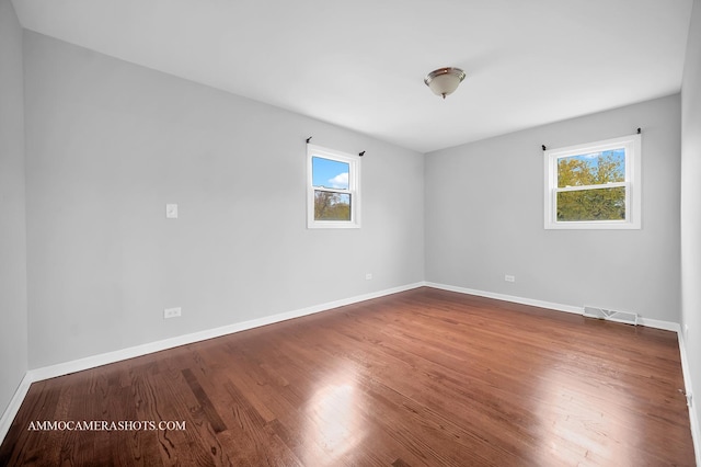 spare room with plenty of natural light, wood finished floors, visible vents, and baseboards