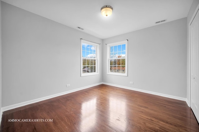 empty room with dark wood-style floors, baseboards, and visible vents