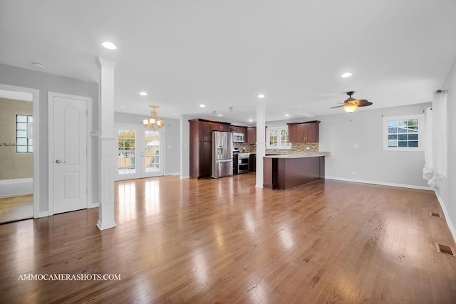 unfurnished living room with ceiling fan with notable chandelier, recessed lighting, a healthy amount of sunlight, and wood finished floors