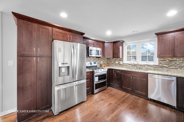 kitchen with light stone counters, backsplash, appliances with stainless steel finishes, a sink, and light wood-type flooring