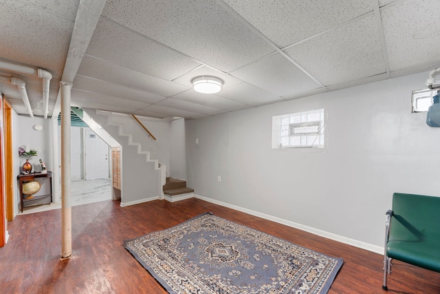 basement with a paneled ceiling, stairs, baseboards, and wood finished floors