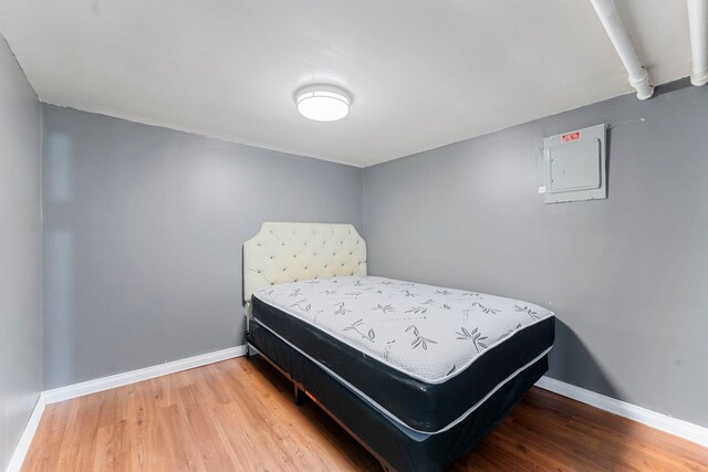 bedroom featuring electric panel, wood finished floors, and baseboards