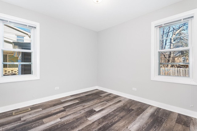 spare room featuring dark wood-type flooring, a healthy amount of sunlight, visible vents, and baseboards