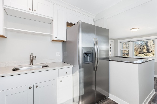 kitchen featuring stainless steel refrigerator with ice dispenser, a sink, open shelves, white cabinetry, and baseboards