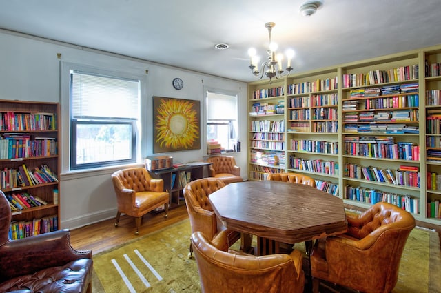 living area with wood finished floors, an inviting chandelier, and wall of books