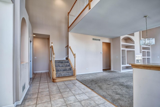 foyer entrance featuring visible vents, baseboards, stairway, light carpet, and a high ceiling