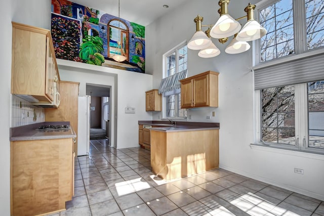 kitchen featuring stainless steel gas cooktop, a peninsula, a high ceiling, a sink, and a chandelier