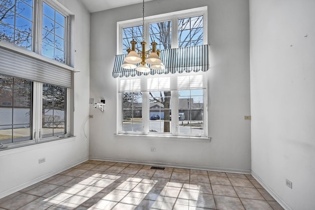 unfurnished dining area with tile patterned flooring, a high ceiling, a notable chandelier, and plenty of natural light