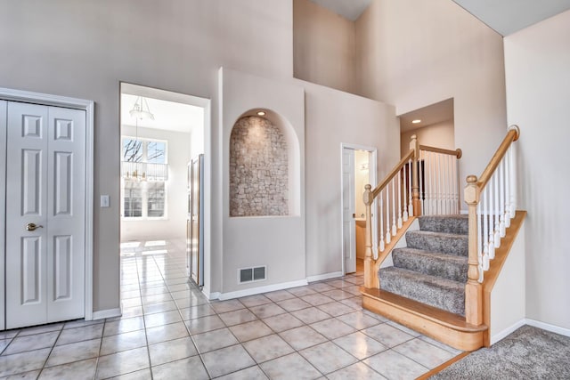 foyer entrance with light tile patterned floors, baseboards, visible vents, a high ceiling, and stairs