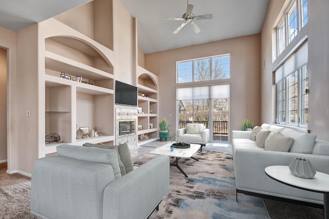 living area with built in shelves, baseboards, ceiling fan, a fireplace, and a high ceiling