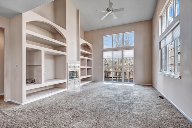 unfurnished living room with built in shelves, baseboards, a towering ceiling, and carpet floors