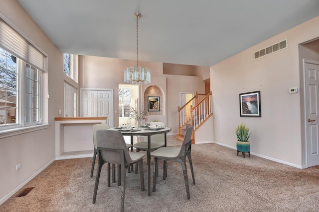 dining area featuring visible vents, carpet floors, an inviting chandelier, and stairway