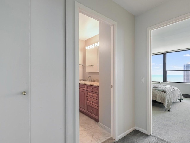 corridor with a sink, baseboards, marble finish floor, and light carpet