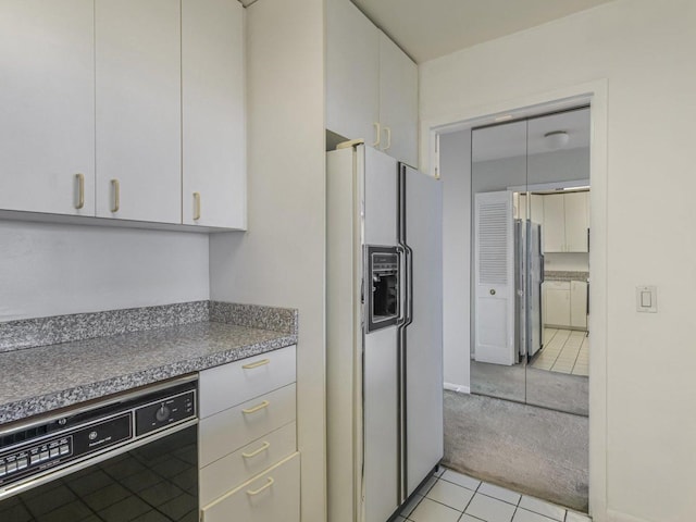 kitchen with light tile patterned floors, white cabinets, black dishwasher, white fridge with ice dispenser, and light colored carpet