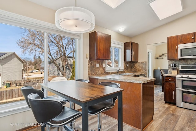 kitchen featuring light wood-type flooring, range with two ovens, vaulted ceiling with skylight, a peninsula, and a sink