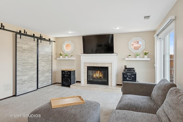 living area with visible vents, a barn door, carpet flooring, and a tile fireplace