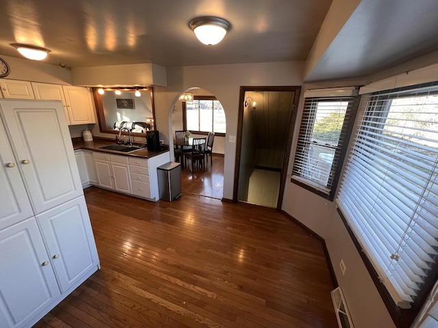 kitchen featuring dark wood-type flooring, a sink, dark countertops, arched walkways, and white cabinets