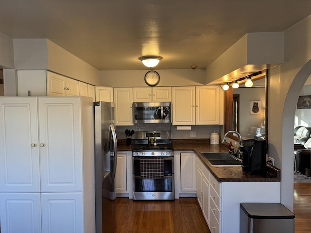 kitchen featuring dark wood finished floors, arched walkways, white cabinets, stainless steel appliances, and a sink