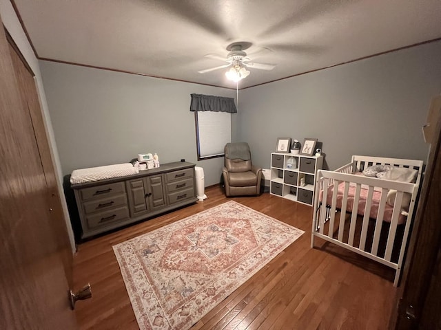 bedroom featuring crown molding, ceiling fan, wood finished floors, a closet, and a nursery area