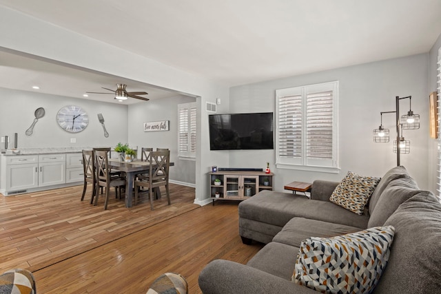 living room featuring visible vents, baseboards, ceiling fan, and light wood finished floors