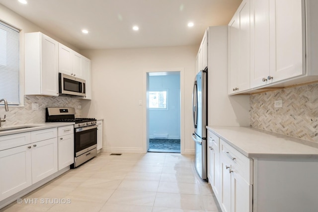 kitchen featuring appliances with stainless steel finishes, white cabinetry, light countertops, and a sink