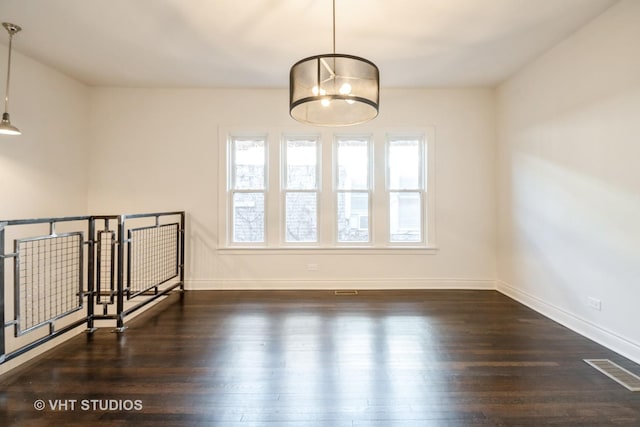 empty room with visible vents, baseboards, wood finished floors, and a chandelier