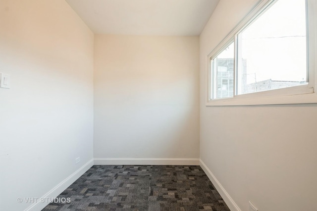 spare room with dark colored carpet and baseboards