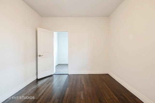 spare room featuring baseboards and dark wood-type flooring