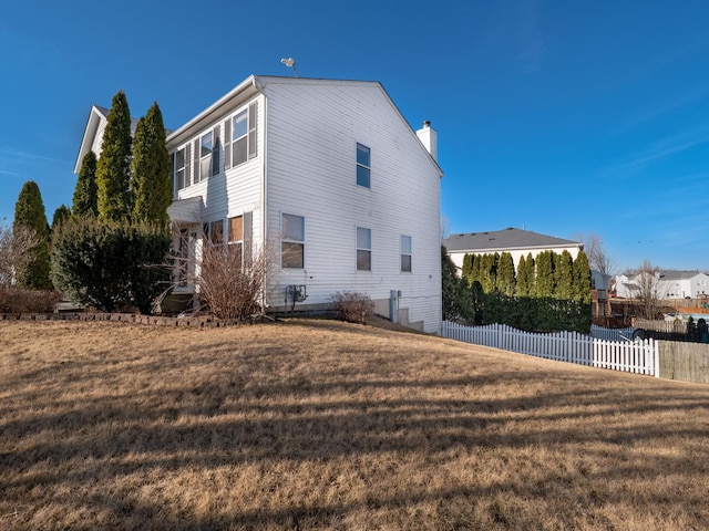 view of side of home featuring a yard, a chimney, and fence