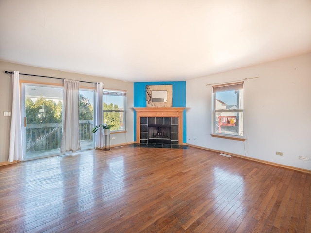 unfurnished living room featuring a tiled fireplace, hardwood / wood-style flooring, visible vents, and baseboards