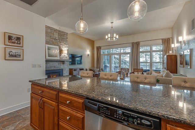 kitchen with brown cabinetry, open floor plan, dishwasher, and a stone fireplace