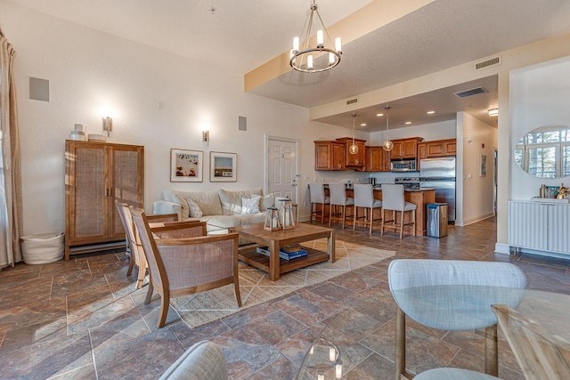 living area featuring an inviting chandelier, stone tile floors, baseboards, and visible vents