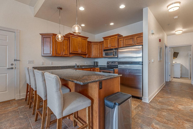 kitchen featuring a kitchen bar, brown cabinets, stone tile floors, stainless steel appliances, and baseboards