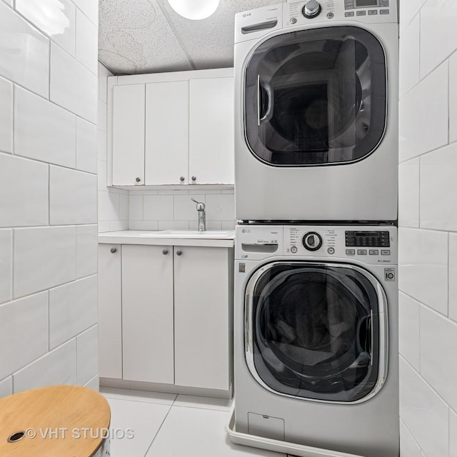 laundry room with light tile patterned floors, cabinet space, tile walls, and stacked washing maching and dryer