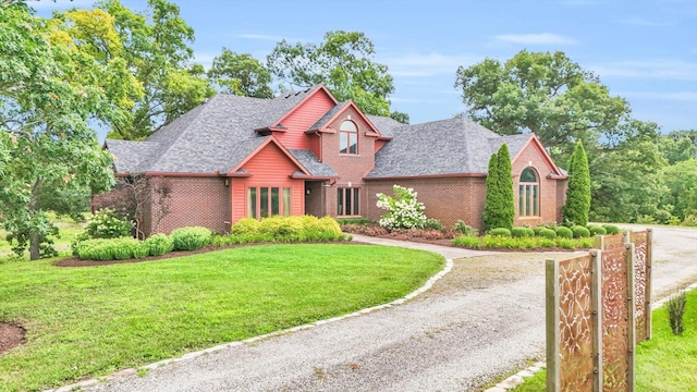 view of front facade featuring driveway, brick siding, a front yard, and a shingled roof