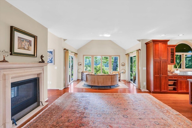 living room featuring light wood finished floors, baseboards, vaulted ceiling, recessed lighting, and a glass covered fireplace