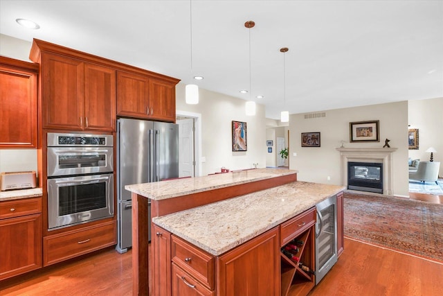 kitchen featuring a kitchen island, a glass covered fireplace, wood finished floors, open floor plan, and appliances with stainless steel finishes