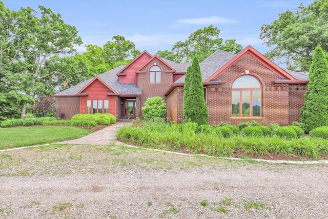 view of front of home featuring a front yard, brick siding, and a shingled roof