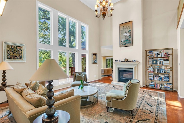 living area with wood finished floors, baseboards, an inviting chandelier, a towering ceiling, and a glass covered fireplace