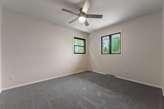 spare room featuring dark colored carpet, visible vents, baseboards, and ceiling fan