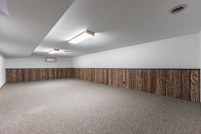 finished below grade area with carpet flooring, visible vents, a wainscoted wall, and wood walls